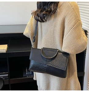 Détail de la pochette en cuir noir avec texture crocodile et poignée anneau métal