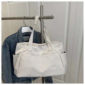 Close-up of a cream canvas tote bag with a fashion leather patch and side pocket