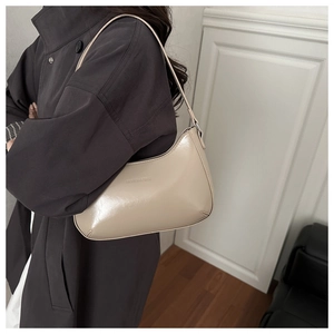 Detail of a beige glossy leather hobo bag worn with a brown coat against a white wall