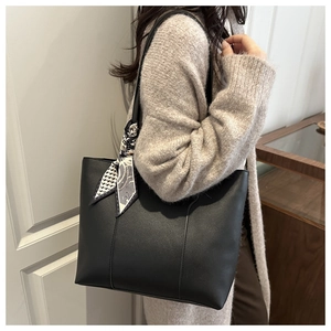 Detail of black faux leather tote bag with vertical stitching and decorative scarf on handle