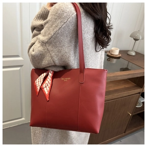 Detail of red leather tote bag with elegant silk scarf handle and golden logo lettering