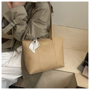 Close-up of beige tote bag featuring gold lettering and checkered silk scarf detail