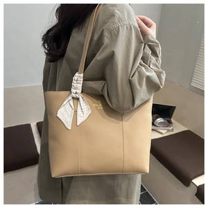 Detail of beige tote bag featuring decorative silk scarf and golden logo lettering