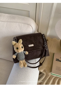 Detailansicht einer dunkelbraunen Vintage-Umhängetasche mit Plüschhase auf dem Sofa