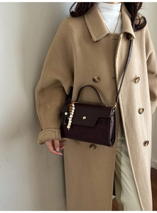Detail of dark brown vintage handbag with a colorful beaded charm on a wool coat
