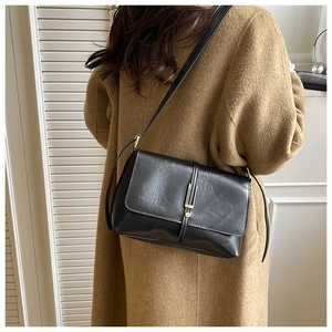 Détail d'un sac bandoulière en cuir noir avec boucle dorée porté par un mannequin en studio