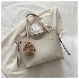 Detail der beigen Shopper-Tasche mit braunem Teddybär-Anhänger auf weißem Bett