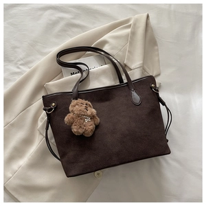 Detail einer dunkelbraunen matten Shopper-Tasche mit Plüschbär-Anhänger auf Sakko