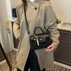 Elegant black leather top handle bag with colorful wooden beads on a stylish trench coat