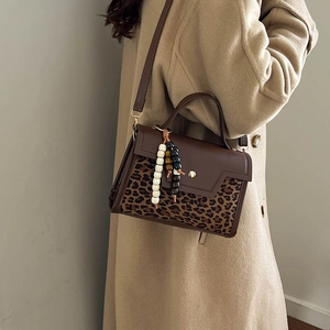 Brown leather handbag with leopard print flap and beaded charm on beige coat
