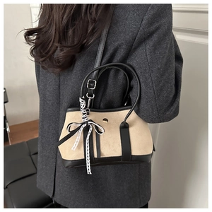 Detail view of two-tone suede handbag with metal buckle and lace bow on a model