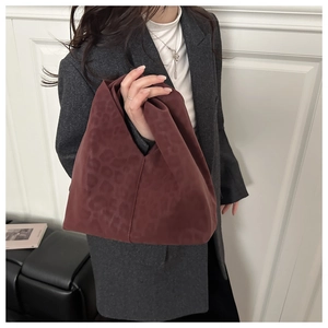 Detail of burgundy leopard print tote bag with knotted handle worn by a model in a gray blazer