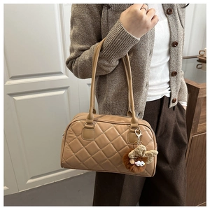 Brown quilted tote bag with cute plush pendant shown on shoulder in cozy indoor setting