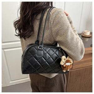 Quilted black tote bag detail featuring a cute plush monster charm on a glossy leather surface