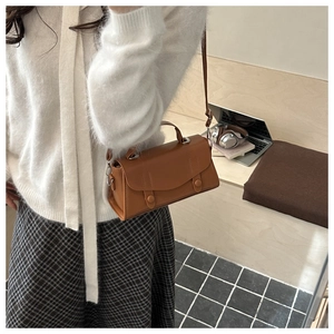 Close-up of caramel leather baguette bag worn crossbody with buckle details