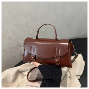 Detail of vintage caramel leather handbag featuring decorative straps and round buckle