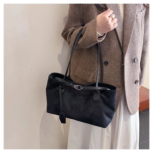 Detail of black suede tote bag with leather buckle strap and pendant on a model