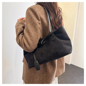 Detailed side view of large black suede tote bag with rectangle tag on tweed blazer