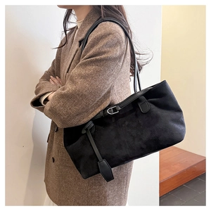 Close-up of black suede tote bag showing the matte texture and shoulder straps on a model