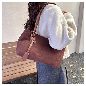 Outdoor shot of a deep brown suede tote bag with leather straps and knot charm detail