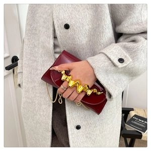 Sac de soirée en cuir verni bordeaux avec poignée dorée et bandoulière sur manteau gris