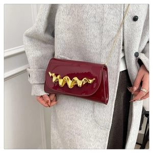 Détail d'un sac en cuir verni bordeaux avec une boucle métallique dorée en forme de vague