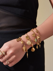 Detail of layered gold-plated bracelets with shell and fish charms on model's wrist