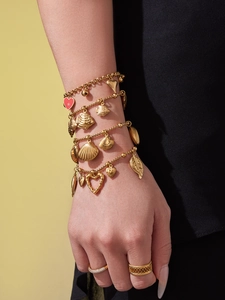 Detail of gold-plated beach charm bracelet with shell, fish, and heart charms on wrist