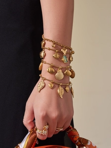 Detail view of gold-plated sea shell and fish charm bracelets with leopard head ring