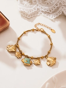 Detail of gold-plated fish charm bracelet with blue enamel in a luxury beach style