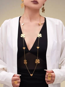 Close-up of a model wearing a gold clover and heart jewelry set with a white shirt
