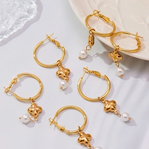 Goldene Kleeblatt Ohrringe mit Perlenanhängern auf einer weißen Texturfläche