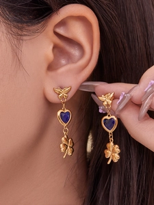 Close-up of gold butterfly earrings with blue heart stone and clover drop on a model
