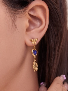 Close-up of dangling gold butterfly earrings with blue heart stone and clover charm