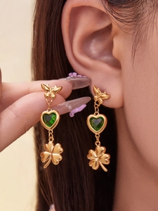 Detail of golden butterfly earring with green heart gemstone and clover pendant
