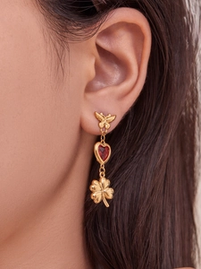 Close-up of gold butterfly earrings with red heart stones and clover charms on a model
