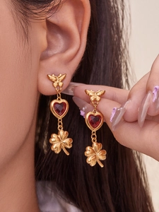 Macro detail of gold butterfly earrings with red heart gems and clover pendants