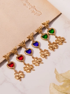 Detail of gold clover earrings with red blue green heart stones on a beige pouch