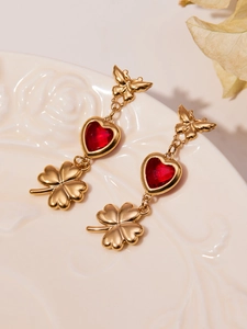 Detailed macro shot of gold butterfly earrings with red heart stones and clover charms