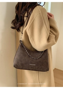 Detail of dark brown hobo bag with silver chain strap shown on a beige coat model
