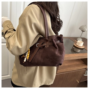 Detail of dark brown suede shoulder bag with smooth leather straps and colorful beaded charm