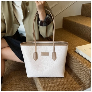 Detail of white tote bag with embossed lettering and brown handles on carpeted stairs