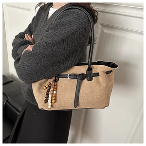 Detail of suede shoulder bag featuring black leather straps and wooden bead tassel