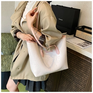 Detailed view of white embossed tote bag with cartoon patterns worn by model in light coat