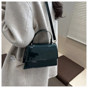 Detail of dark green patent leather trapezoid handbag with gold rivets on model coat