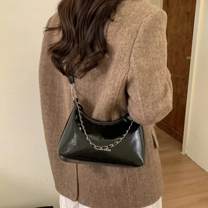 Sac à bandoulière noir brillant minimaliste avec chaîne en métal porté par un mannequin