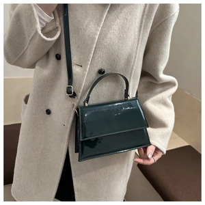 Detail of dark green patent leather crossbody bag with top handle and gold hardware