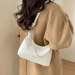 Sac hobo minimaliste en cuir blanc avec chaîne argentée porté sur un manteau en laine