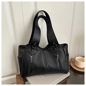 Close-up of black leather tote bag featuring decorative zippers and soft lychee texture