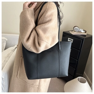 Detail of black pebbled leather tote bag with embossed fashion text on camel coat